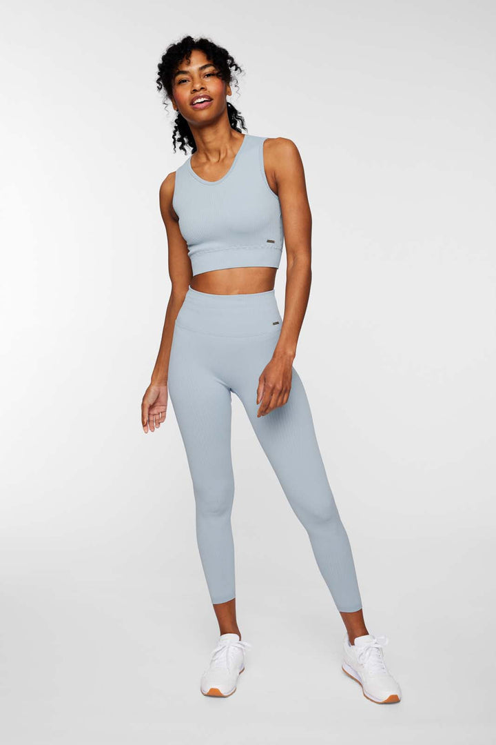 A woman standing in a pose that showcases the fit of seamless ribbed leggings, solid color, light blue, paired with a matching ribbed sports bra.